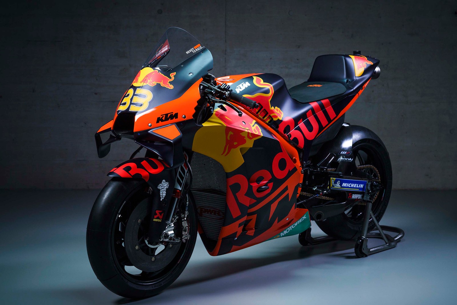 A close up of a motorcycle parked in a garage with a red bull logo on the side (ktm rc16, motogp, red bull racing, 2021, bikes)