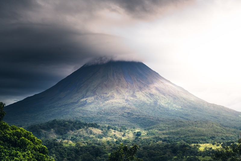 Imagem desfocada de uma montanha com uma nuvem no céu e árvores (vulcão arenal, viagem, aventura, nuvem, montanha)