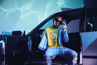 Rapper em amarelo e denim posando ao lado de um carro clássico