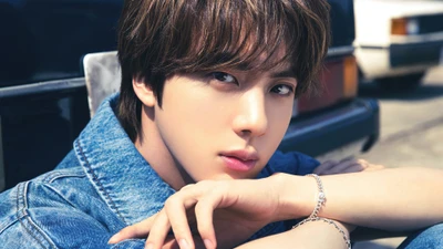 Jin from BTS, showcasing a captivating gaze in a casual denim outfit.