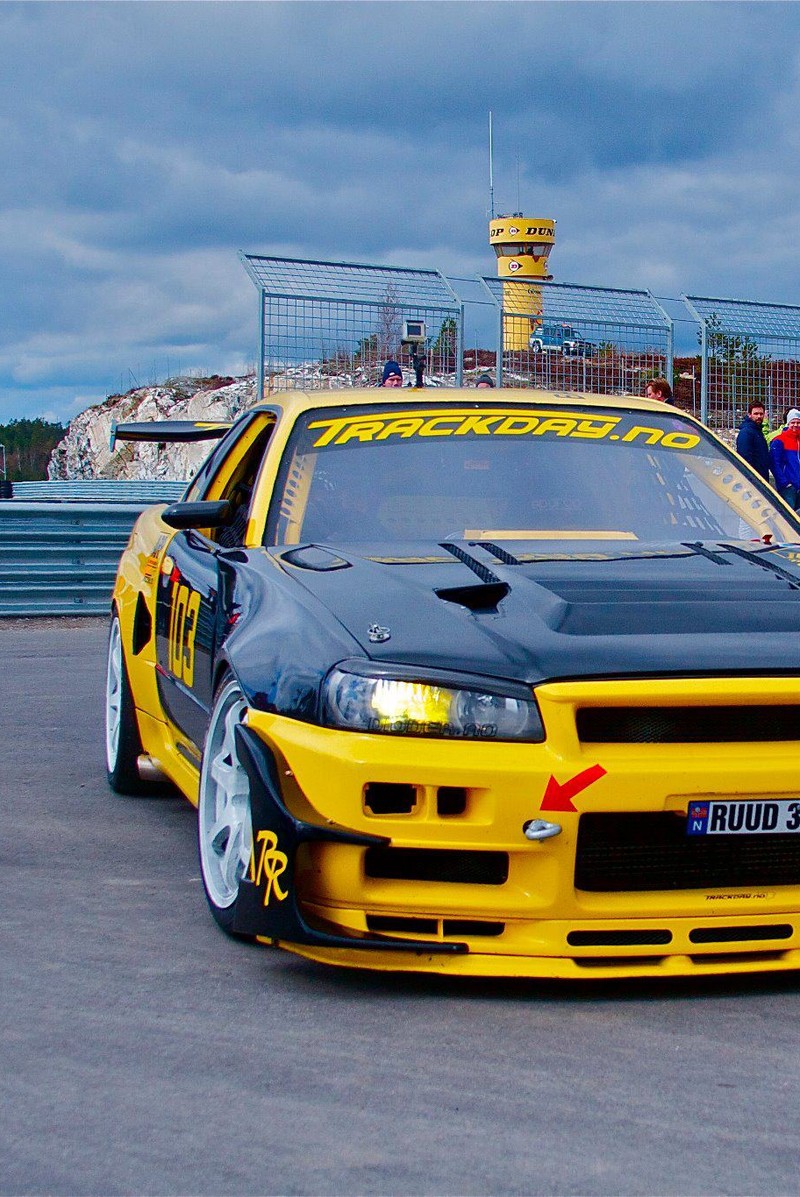 Un coche amarillo con capó y parachoques negros estacionado en una pista (coches, deriva)