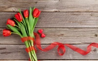 Ramo de tulipanes rojos atado con una cinta, acompañado de pequeñas decoraciones en forma de corazón sobre una superficie de madera rústica, perfecto para expresar amor y afecto.