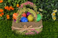 Colorful Easter eggs nestled in a decorated wicker basket surrounded by vibrant spring flowers and lush grass.