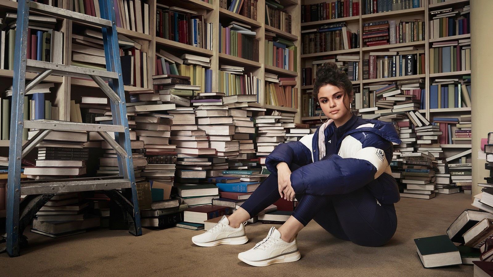 Una mujer sentada en el suelo frente a una pila de libros (selena gomez, cantante, celebridad, mujeres, chicas)