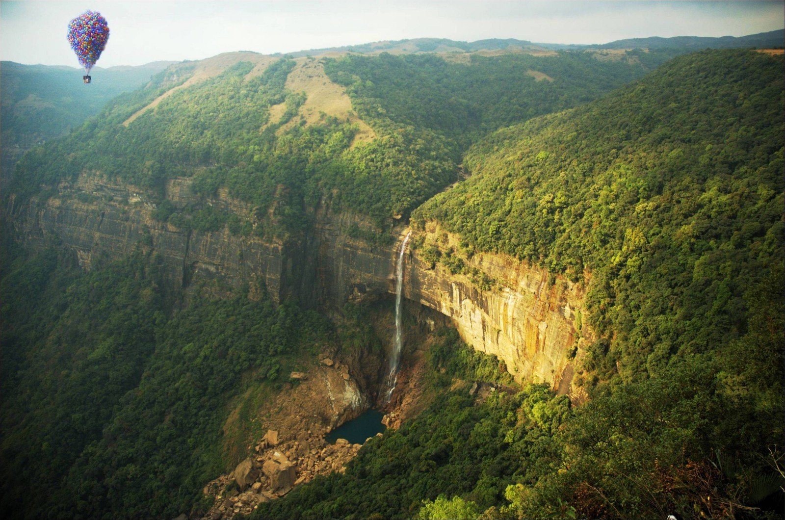 A view of a hot air balloon flying over a waterfall (waterfall, hill station, vegetation, highland, mountain)