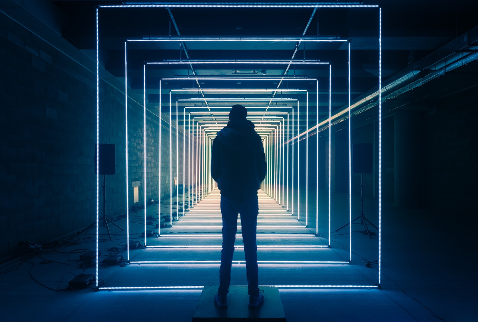 Ein mann steht in einem tunnel mit neonlichtern an den seiten (fluchtpunkt, blaue lichter, person, geometrisch, form)