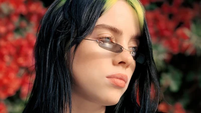 Billie Eilish mit auffälligen grünen Strähnen, trägt Sonnenbrille vor einem lebhaften floralen Hintergrund.