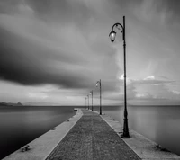 Chemin solitaire sous un ciel nuageux : Un quai maritime en noir et blanc