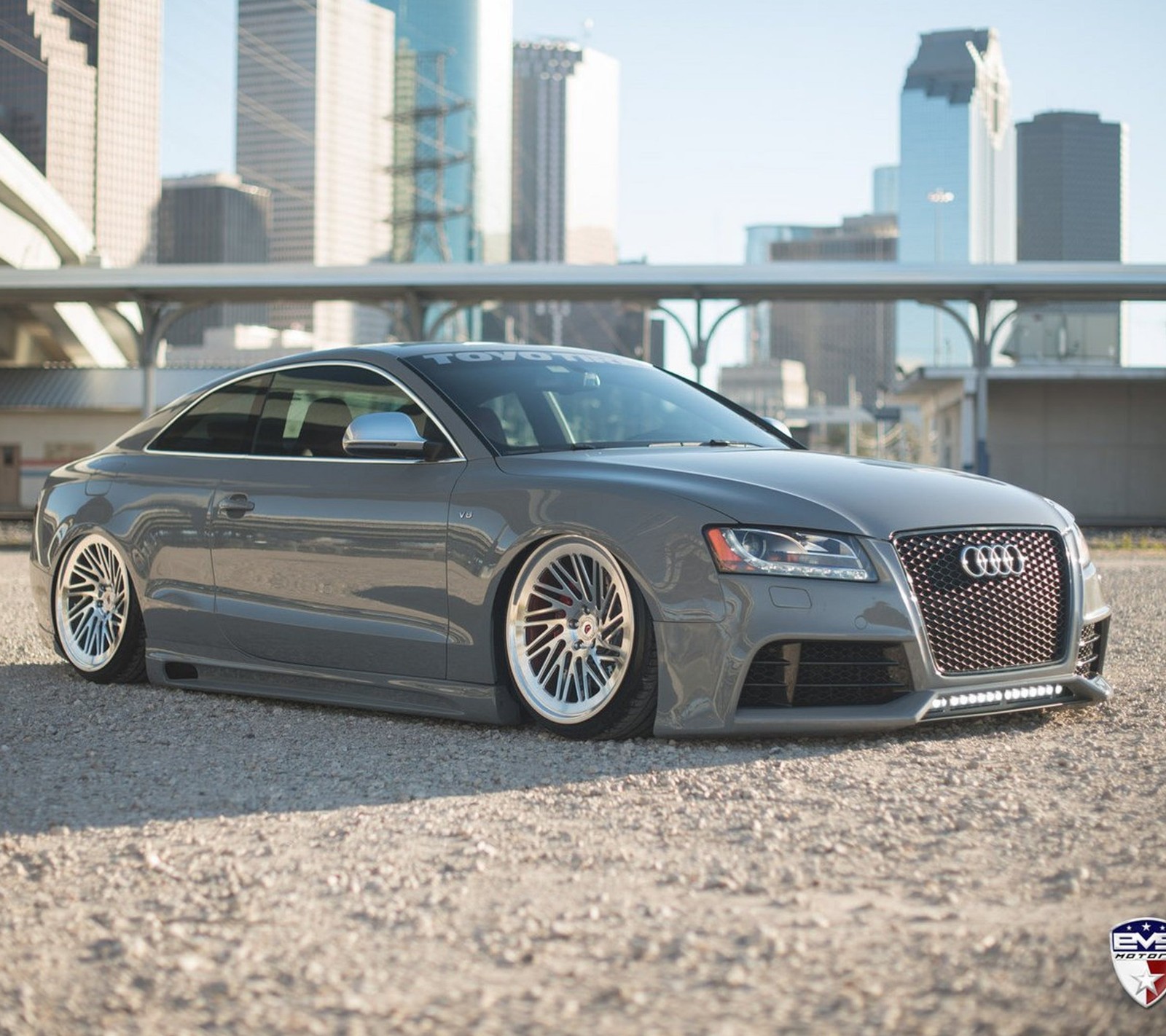 Un audi gris estacionado frente a un horizonte urbano. (audi, coche, modificado)