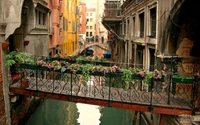 Balcão pitoresco adornado com flores vibrantes com vista para um canal sereno em Veneza, Itália, perto da icônica Ponte de Rialto.