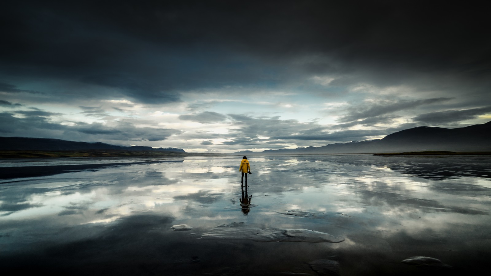 Une personne se tenant sur la plage avec une planche de surf dans l'eau (plage, solo, nuageux, ciel, paysage)