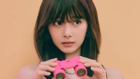 Tzuyu holding pink binoculars against a vibrant orange backdrop.