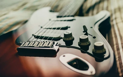 Close-up of a Fender electric guitar showcasing its intricate controls and polished body on a textured surface.