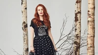 Madelaine Petsch em um traje preto e branco estiloso, cercada por bétulas.