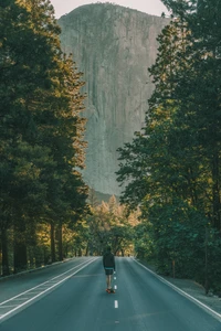 Skateboarding through a serene forested road with towering cliffs and vibrant greenery.