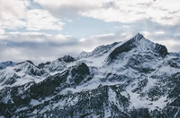 Schneebedeckte Bergkette unter einem bewölkten Himmel, die raues Terrain und einen dramatischen Gipfel zeigt.