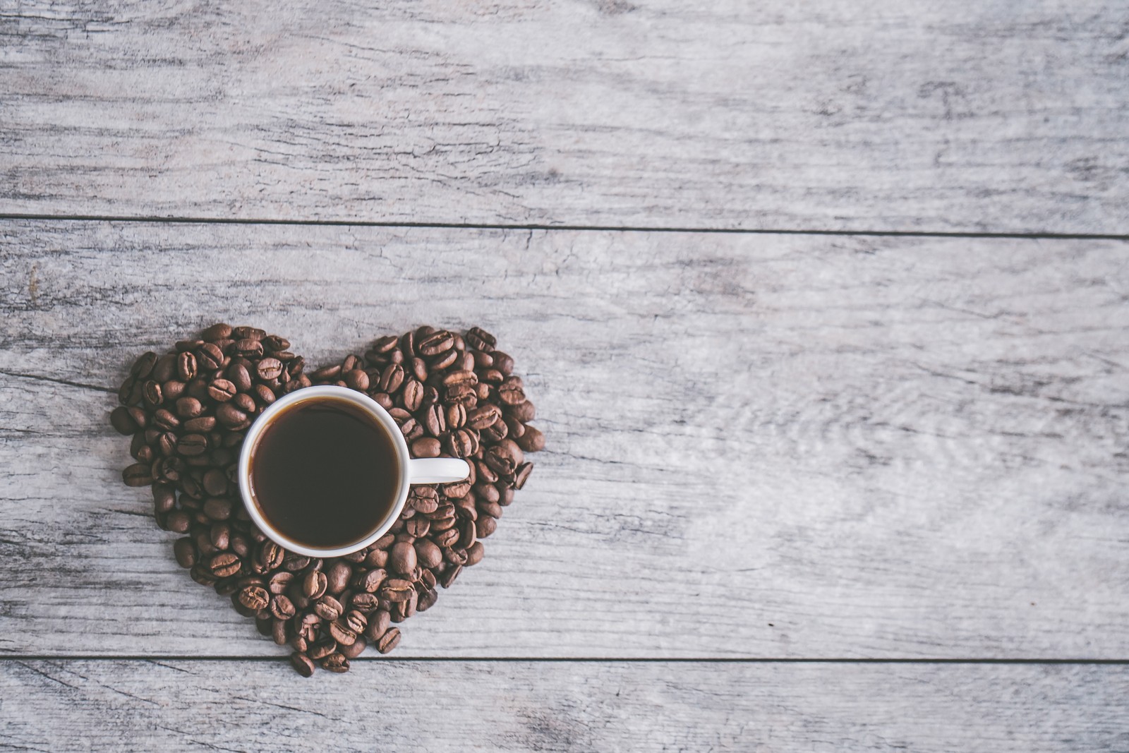 Nahaufnahme einer tasse kaffee mit kaffeebohnen in herzform (kaffee, kaffeetasse, tasse, koffein, herz)