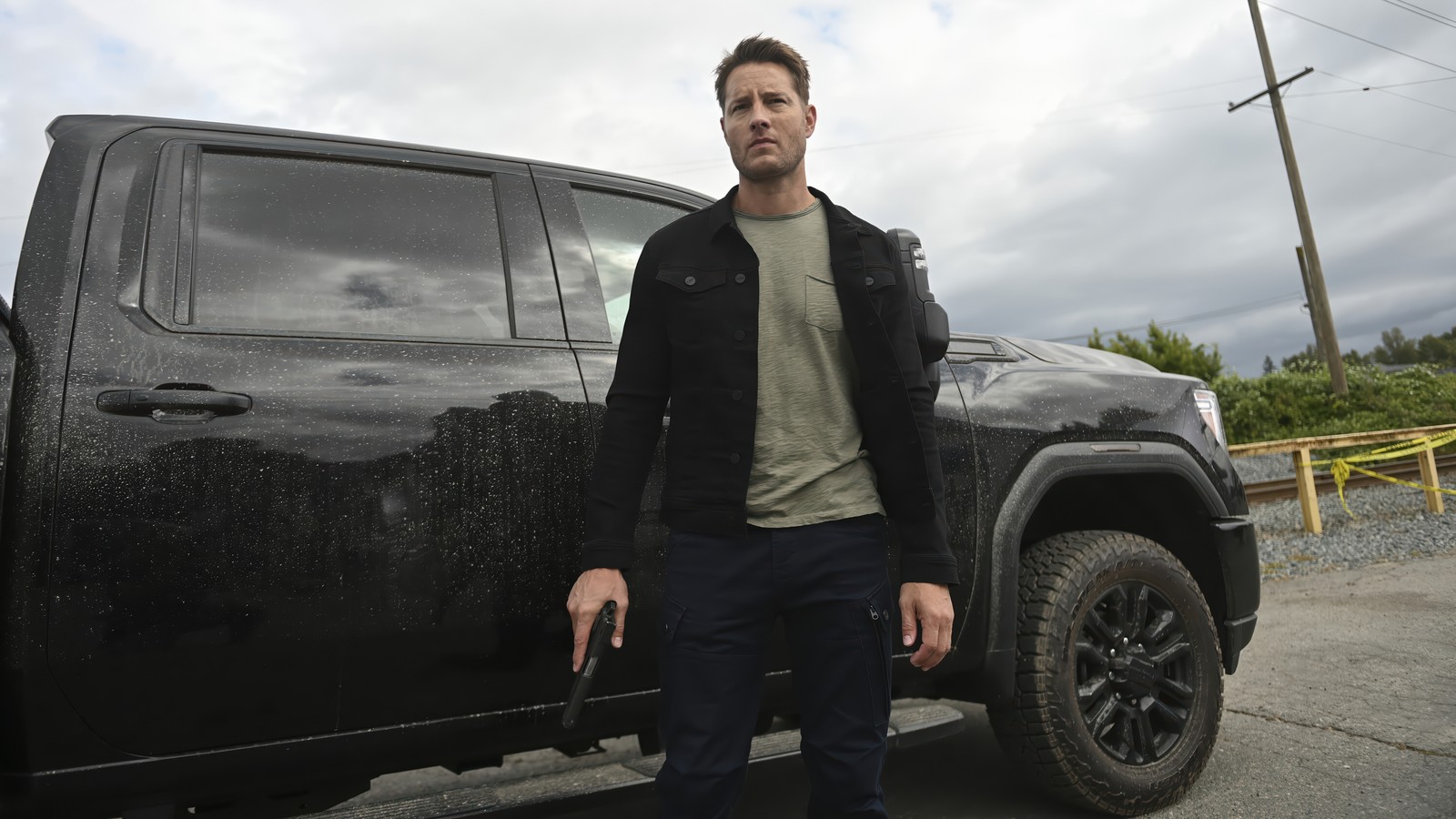 Homme arabe se tenant devant un camion noir avec une arme (série tracker, tracker series, série télévisée, justin hartley)