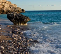 Costa tranquila com afloramento rochoso e ondas suaves