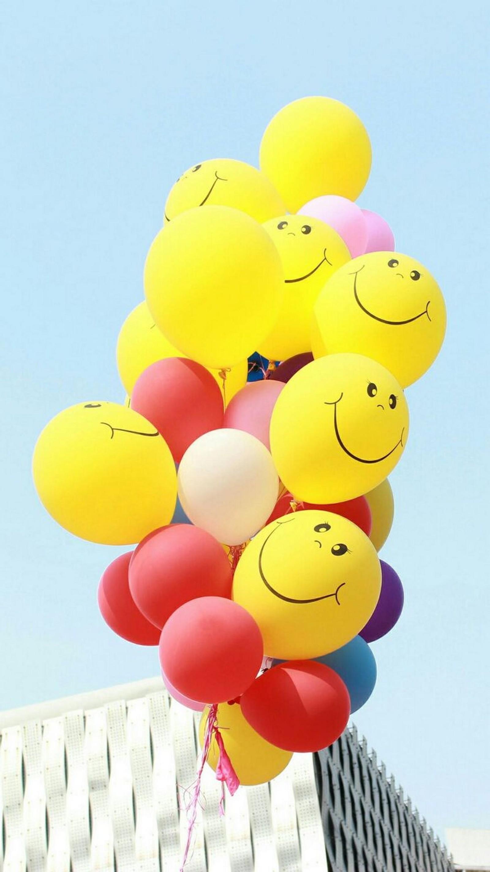 There are many balloons with smiley faces on them being held by a man (balloon, face, fly, happy, love)