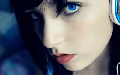 Close-up of a girl with striking blue eyes and vivid lips, wearing headphones, showcasing beauty and creative expression.