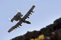 Aerial view of a military aircraft maneuvering above rocky terrain, showcasing its distinctive propeller-driven design.