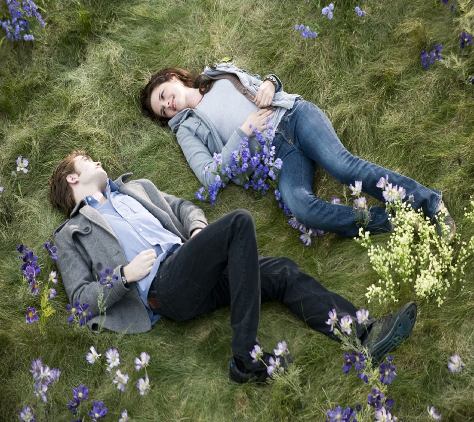 Deux personnes allongées dans l'herbe avec des fleurs dans les mains (couple, mignon, amour, romantique, crépuscule)