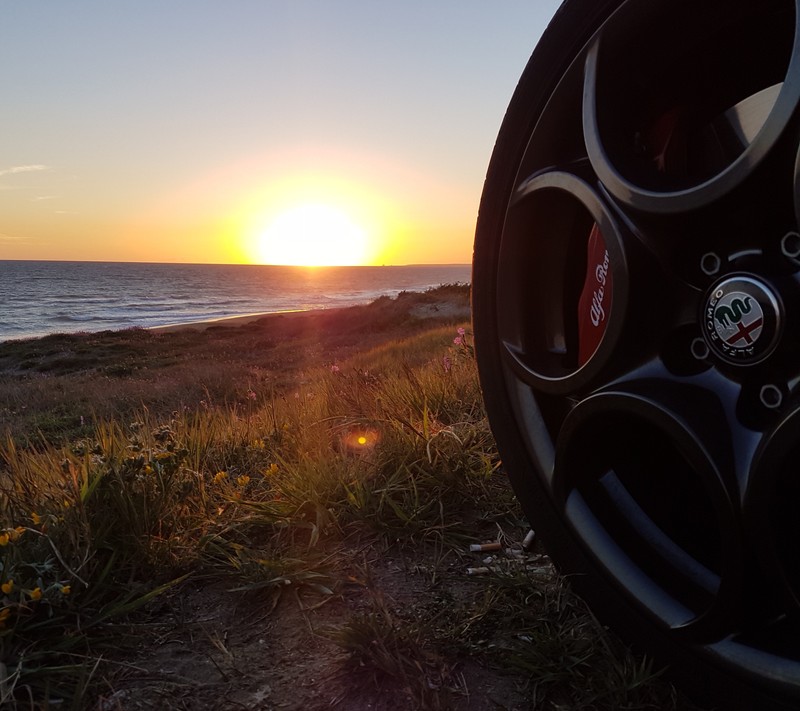 Ein verfälschter blick auf einen reifen mit einem sonnenuntergang im hintergrund (5fori, alfa romeo, brembo, giulietta, lameccanicadelleemozioni)