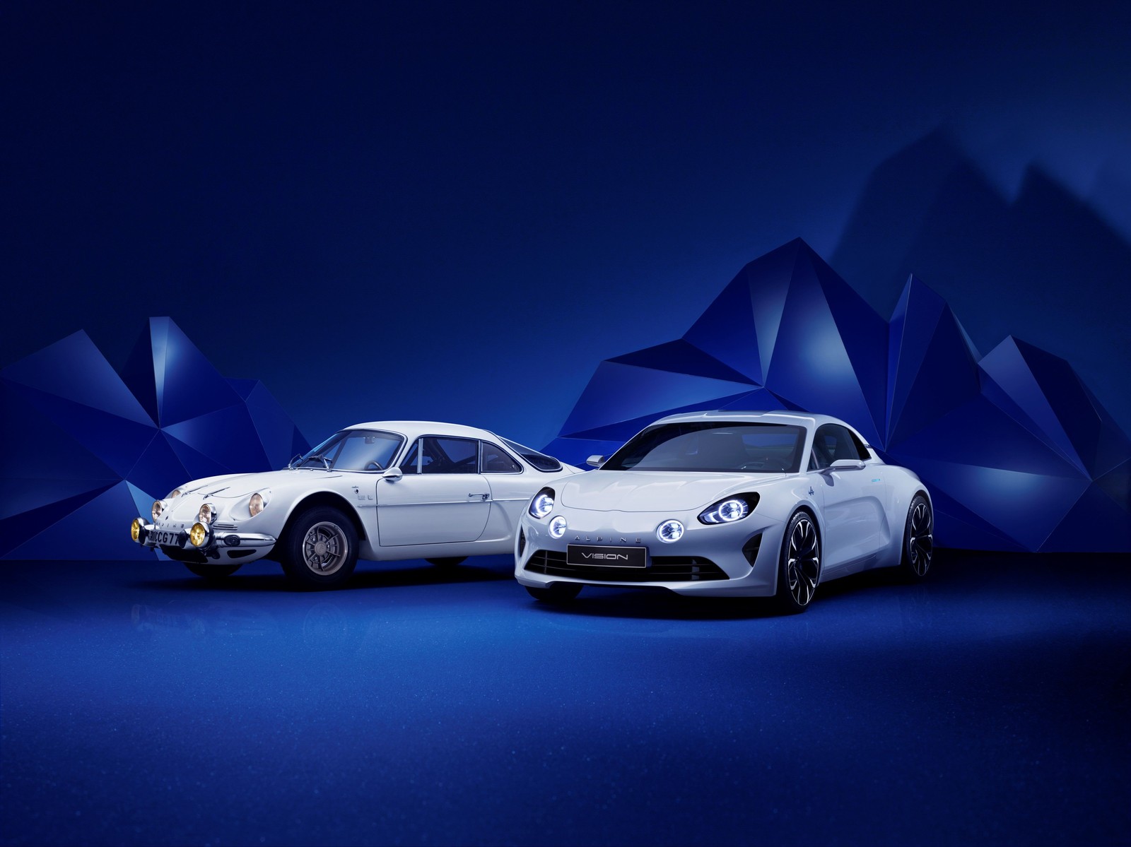 Two white cars are parked in front of a mountain (renault, sports car, car, supercar, automotive lighting)