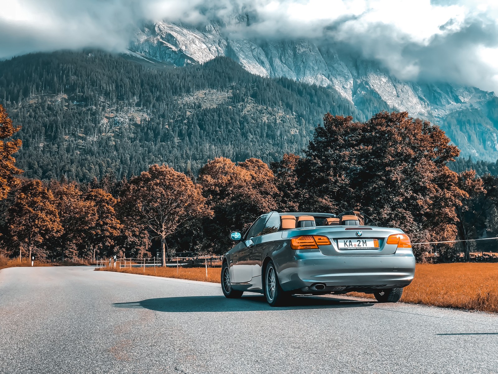 Un primer plano de un coche conduciendo por una carretera con montañas al fondo (coche, bmw, bmw 320, convertible, bmw serie 3 e46)