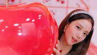 Jisoo of BLACKPINK playfully poses with a giant cherry in a colorful, vibrant setting.