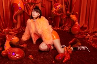 Charli XCX in a vibrant orange setting, featuring playful, organic forms and a bold fashion statement that blends performance art with pop music aesthetics.