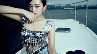 Yujin from IVE showcasing a chic silver outfit on a boat with a city skyline in the background.