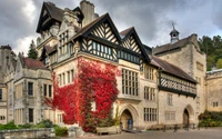 Stately English country house with striking medieval architecture and vibrant red ivy adorning the facade.