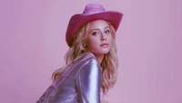 Lili Reinhart con un elegante sombrero rosa y un atuendo brillante contra un fondo pastel.