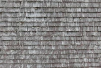 Weathered wooden roof tiles arranged in a textured pattern against a stone wall backdrop.