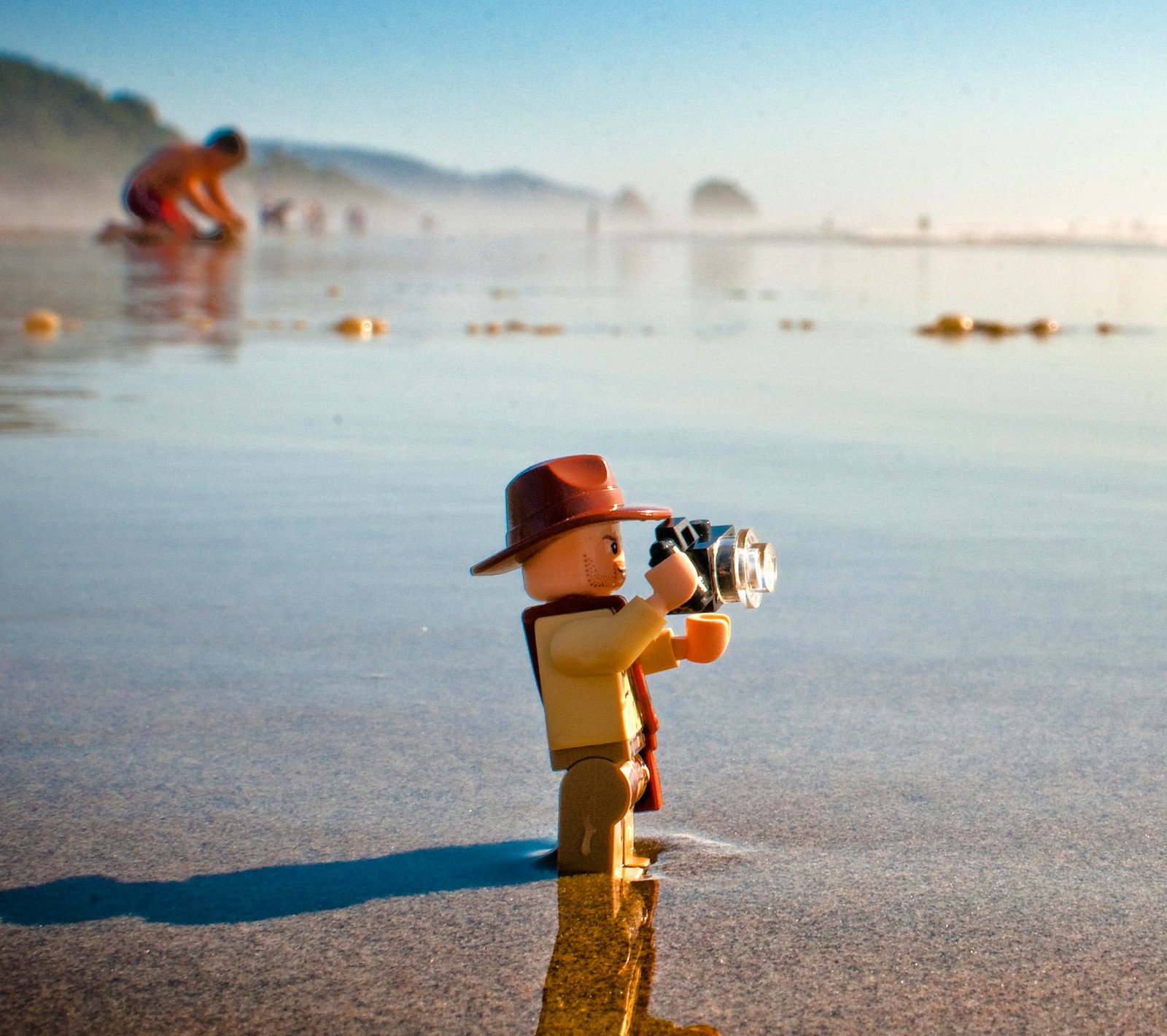 Un homme lego avec une caméra sur la plage avec des gens en arrière-plan (amusement, jeux, lego, gens)