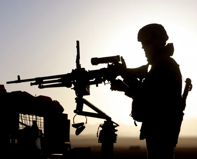 Soldado en silueta operando una ametralladora al atardecer.