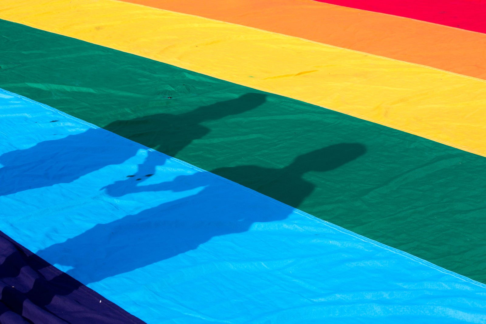 Schatten von zwei personen auf einer regenbogenfarbenen oberfläche (blau, grün, turquoise, gelb, azurblau)