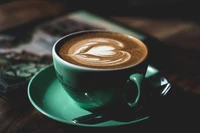 Cappuccino com arte latte de coração em uma xícara verde menta sobre uma mesa de madeira.