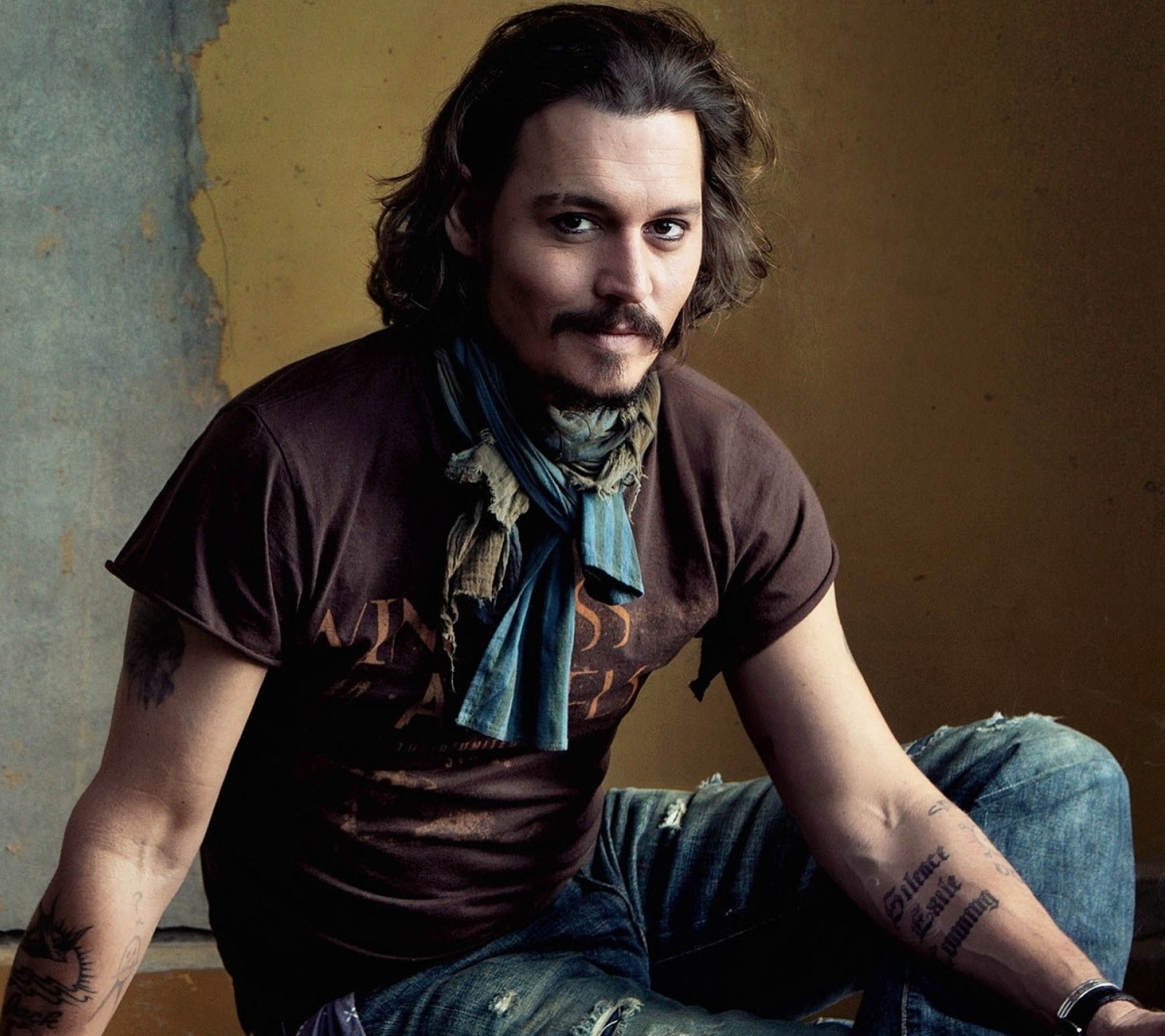 Hay un hombre con bigote y bufanda sentado en una silla (actor, johnny depp)