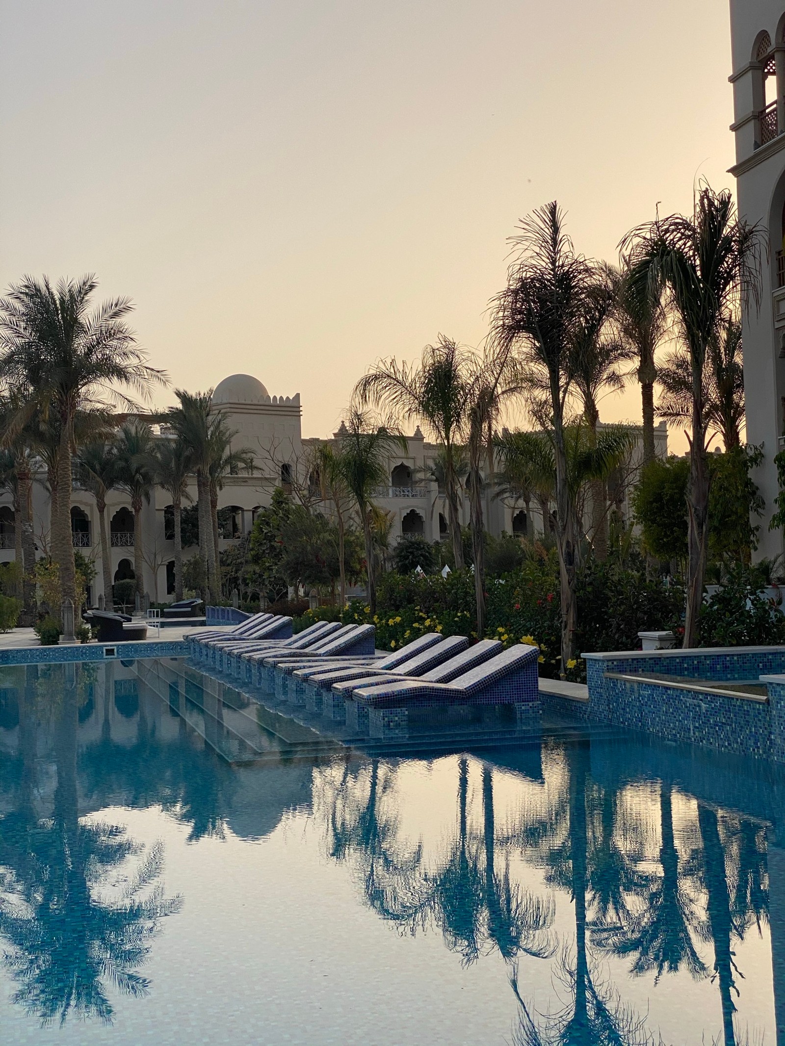 Há muitas espreguiçadeiras na piscina de um hotel (reflexo, água, planta, edifício, piscina)