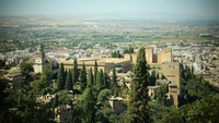 Aerial view of a lush residential area with historic architecture, surrounded by greenery and rolling hills under a clear sky.