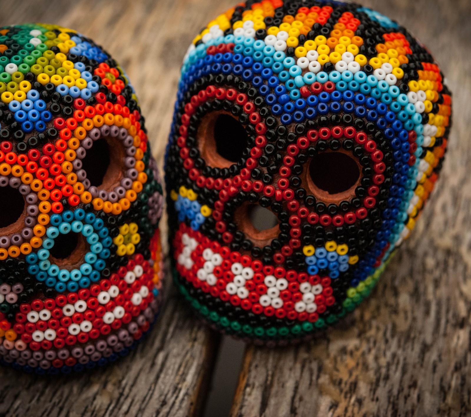 Dos calaveras de cuentas coloridas sentadas en una mesa de madera (darkdroid, calavera, calavera de azúcar)