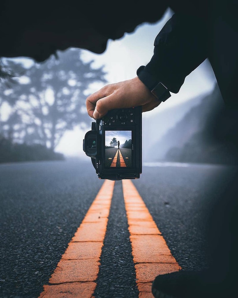 Alguém tirando uma foto de uma pessoa segurando uma câmera na estrada (barricada, transformador, verão, estrada, preto)