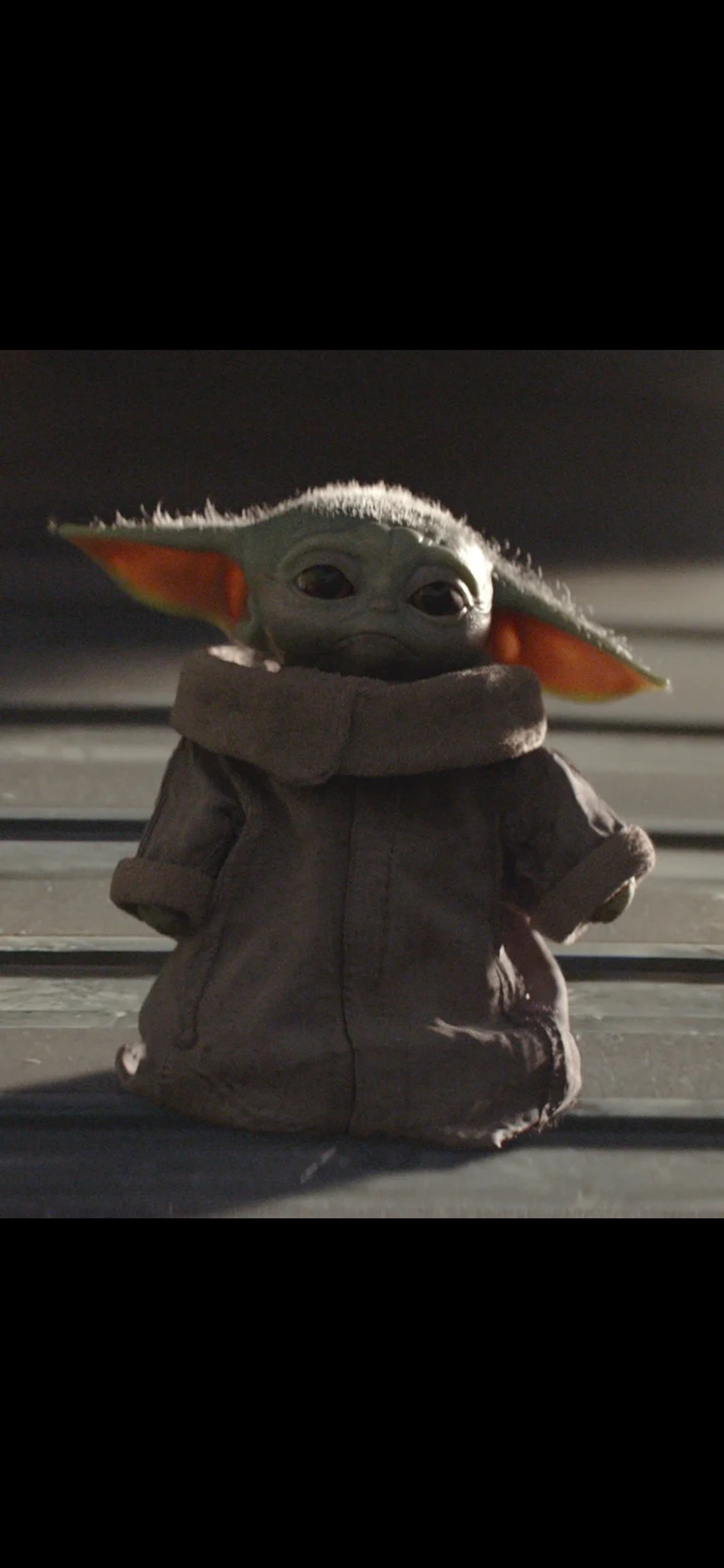 Baby yoda en una chaqueta marrón sentado en un suelo de madera (bebé yoda, baby yoda, mandaloriano, yoda)