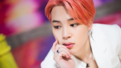 Jimin do BTS com cabelo rosa, exibindo uma expressão pensativa.