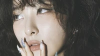 Seulgi de Red Velvet, mostrando una expresión serena con uñas elegantes y cabello ondulado.