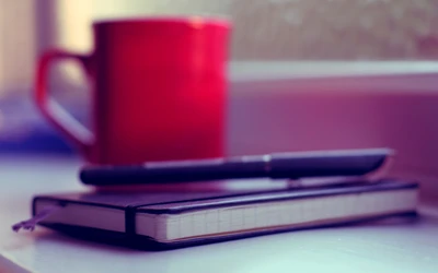 Cuaderno morado con bolígrafo y taza roja en el alféizar de la ventana