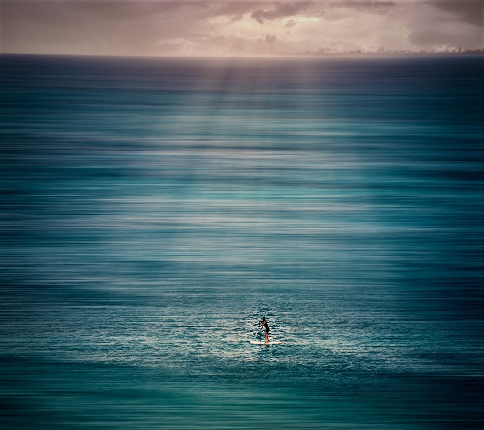 Un surfista en el océano con un cielo nublado y una ciudad de fondo (abej, beograd, recreación)